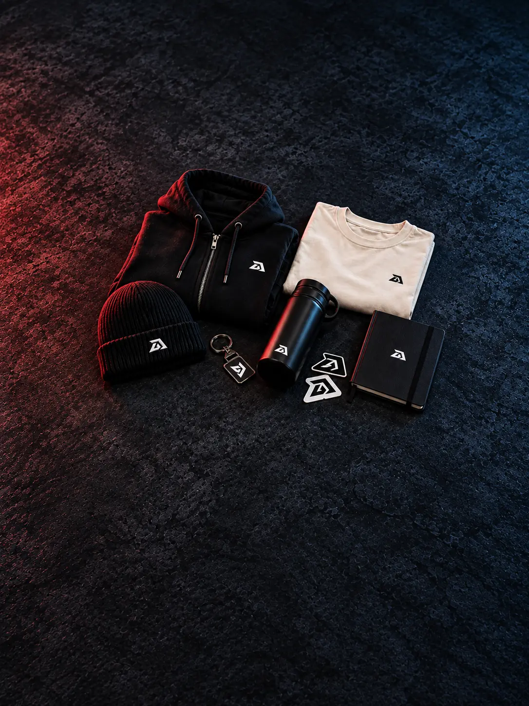 Darukai merchandise collection arranged on a continuous dark studio background: hoodie, cream T-shirt, beanie and accessories